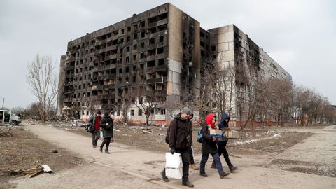 Un grupo de personas camina cerca de varios edificios bombardeados en Maripol