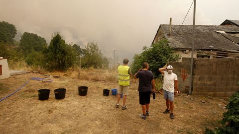 Vecinos de Alvaredos junto a unos capazos llenos de agua y con el humo del incendio al fondo
