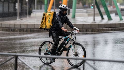 Un repartidor de Glovo, en pleno reparto y bajo la intensa lluvia, en una calle del noroeste de la ciudad de Madrid.