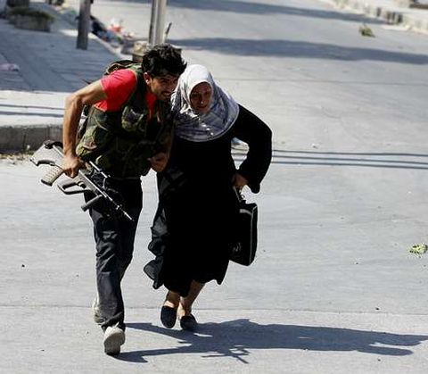 Un joven ayuda a una mujer en medio de combates en Alepo.