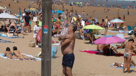 Un hombre se refresca en una ducha en la Playa de San Lorenzo, en Gijn
