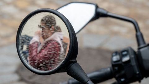 En la foto, el reflejo de una persona en el espejo de una motocicleta