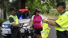 Un agente de la Guardia Civil entrega un chaleco reflectante a una ciclista este lunes en Reza (Ourense)