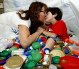 Mat�as con su madre en medio de una de las cajas de tapones que han recogido. 