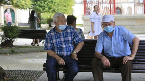 Gente mayor resguardada del sol en los bancos de la Praza Maior a la sombra