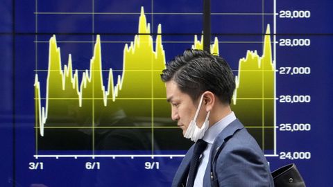 Un hombre consulta su m�vil mientras pasa delante del gr�fico del mercado de Bolsa en Tokio