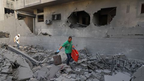 Un paramédico lleva una camilla, mientras los palestinos inspeccionan los daños en un barrio residencial, luego de una operación israelí en Ciudad de Gaza.