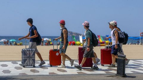 Personas con maletas andando delante de una playa.