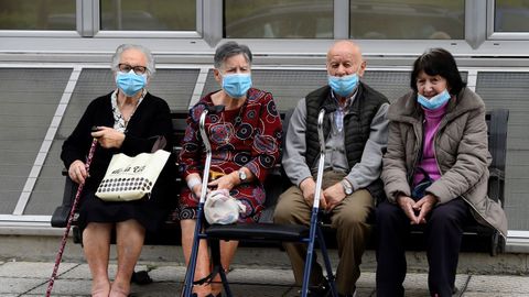 Varias personas mayores toman el sol sentados en un banco en una residencia del ERA, en Asturias
