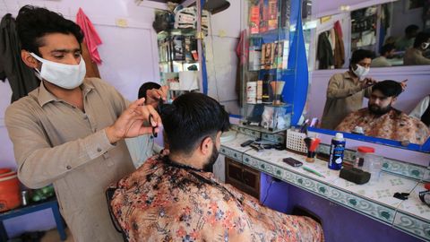 Un peluquero con mascarilla afeita a su cliente despus de que algunas empresas pudieran operar, en Peshawar, Pakistn