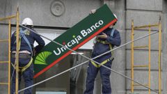 Operarios sustituyen la cartelera y los antiguos logotipos de lo que fuera LiberBank por los nuevos de Unicaja Banco en la sede central en Oviedo