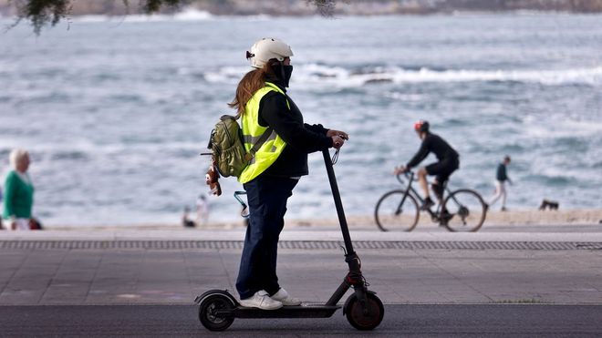 Imagen de una conductora de patinete con casco y chaleco reflectante.