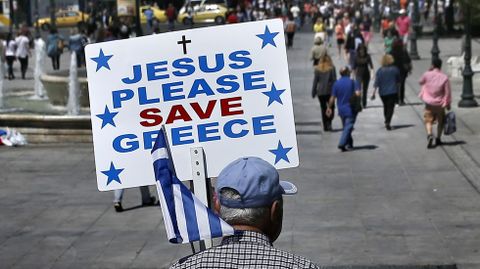 Un hombre pasea por la plaza de Syntagma de Atenas con un cartel que apela a la ayuda divina para Salvar a Grecia. 