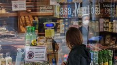 Una mujer observa el escaparate de una tienda de productos t�picos, cuyo cartel informa sobre la entrada limitada en el local, en Oviedo.