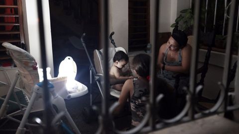 Una mujer conversa con sus hijos con la luz de una lmpara durante un apagn.