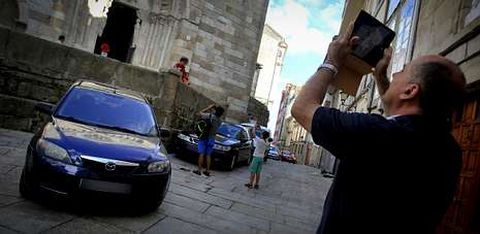 Turistas fotografiando ayer la iglesia de Santiago, con coches aparcados por todo su permetro. 