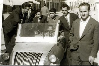 Un grupo de personas posan divertidas alrededor de un Biscuter, en la plaza de Santa Ana de Chantada, en 1960