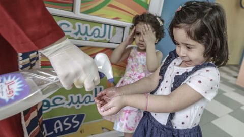 En Gaza, una mujer palestina rocía desinfectante en las manos de unas niñas, una vez que se ha decretado la reapertura de algunos comercios y espacios públicos