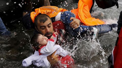 Un refugiado sirio se aferra a sus hijos mientras lucha para salir de un bote en la isla griega de Lesbos
