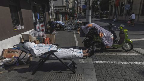 Un repartidor duerme la siesta en una calle de Shangh�i sin quitarse el traje de protecci�n contra el covid