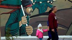 Una familia camina ante un mural en Teher�n, la capital de la rep�blica isl�mica