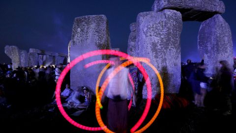 Un joven hace malabares de luz mientras espera la salida del sol durante el festival del Solsticio de Verano en el monumento de Stonehenge, en Reino Unido