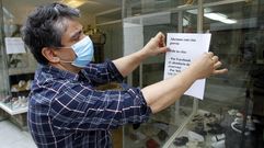 El propietario de una tienda de calzado infantil cuelga el cartel de apertura con cita previa en su local