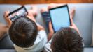 Dos nios consumen contenidos digitales en dos dispositivos mviles
