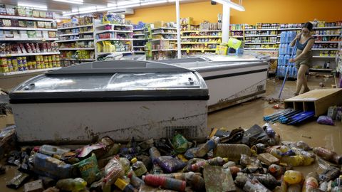 Una mujer retira el lodo acumulado en su comercio en Picanya