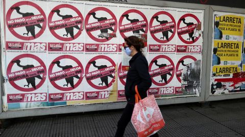 Una ciudadana camina por una calle de Buenos Aires junto a carteles que instan a no pagar la deuda al FMI