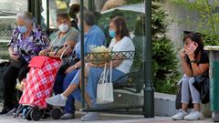 Una mujer fuma junto a la parada de un autob, en el centro de Oviedo, mientras en la marquesina un grupo de ususarias se protege con mascarillas. 