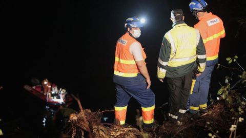 Dos sanitarios y un guardia civil observan desde la orilla cmo los bomberos rescatan desde una lancha el rescate del cuerpo del camionero