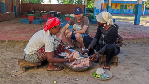 scar departiendo con las cocineras que preparan el pollo para la cena de los visitantes. Detrs se ve el comedor y un poco del cole de Ndungu Kebbeh