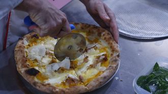 Un hombre corta una pizza con un cortador de acero inoxidable. 