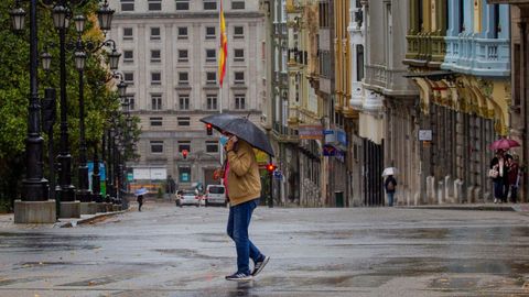 Un hombre camina bajo la lluvia en el centro de Oviedo