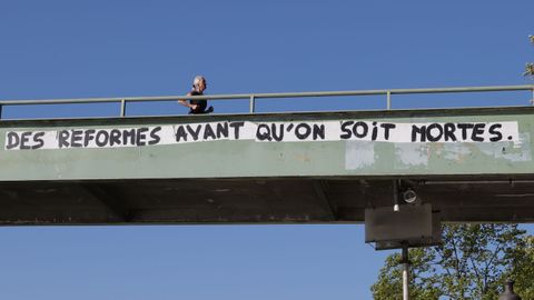 Una mujer hace deporte por un paso elevado en el que se lee una pancarta reivindicativa en Pars, Francia