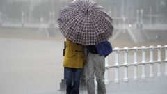 Dos personas comparten paraguas bajo la lluvia este viernes, en la Playa de San Lorenzo, Gijn