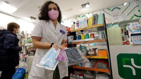 La farmacéutica Blanca González Herrero, la vocal de Dermofarmacia del Colegio de Farmacéuticos de A Coruña (COFC), muestra unos paquetes de mascarillas quirúrgicas y FFP2