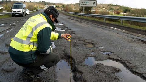Asfalto destrozado. En esta foto de mayo del 2018 se ve a un guardia civil midiendo la profundidad de uno de los socavones que haba entonces en la N-540 junto a Chantada