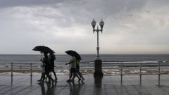 Varias personas se protegen con el paraguas de la lluvia, en el paseo de muro de la playa de San Lorenzo de Gij�n