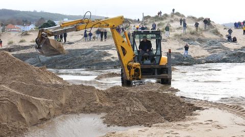 Trabajos de apertura del canal con una excavadora en la playa de Valdovio, seguidos con expectacin desde las dunas.