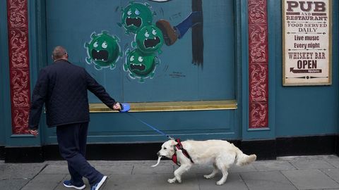 Un hombre pasea a su perro por una calle de Dubln en la que hay pintado un mural sobre el covid-19