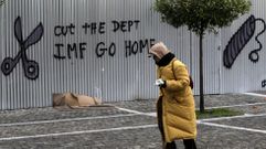 Una mujer pasa ante un grafiti en el que se lee �Rebaja la deuda. FMI vete a casa� en una valla de la Academia de las Ciencias de Atenas.