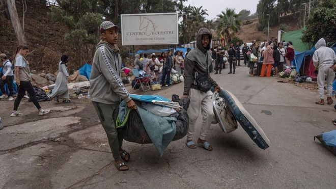 Dos migrantes cargan en Ceuta con sus pertenencias.