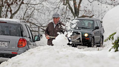 un vecino del pueblo de Pajares trata de sacar su coche tras la nevada