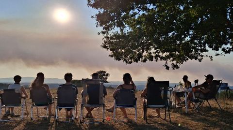 En la foto, un grupo de turistas belgas sigue el eclipse el mi�rcoles en Taboada, con el cielo medio cubierto por el humo de este incendio