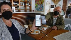 Dos turistas asturianos, mostrando su certificado de vacunaci�n en una cafeter�a de Sanxenxo para poder desayunar en su interior 