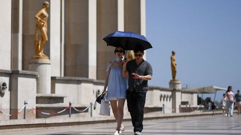 Varias personas se protegen del sol bajo un paraguas cerca de la Torre Eiffel.
