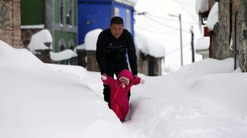 Una nia da sus primeros pasos con ayuda de su padre,  sobre la nieve acumulada en las calles del pueblo asturiano de Pajares.