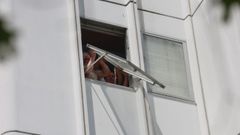 Un vecino sujeta una ventana a punto de descolgarse en su vivienda de la plaza Luis Seoane